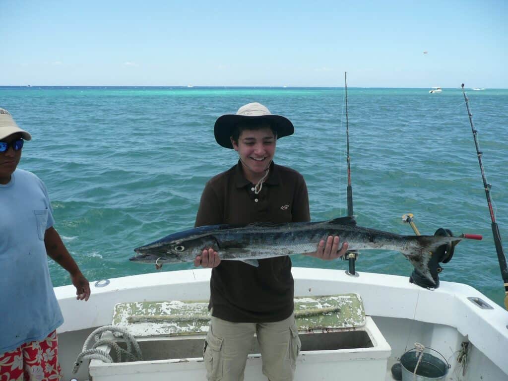 Angler on a private yacht reeling in a fish with clear blue waters around Cozumel